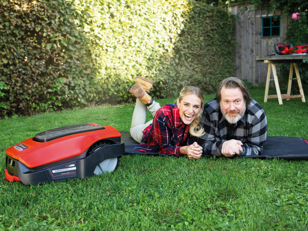 A woman and a man lie on the lawn next to the robot lawn mower