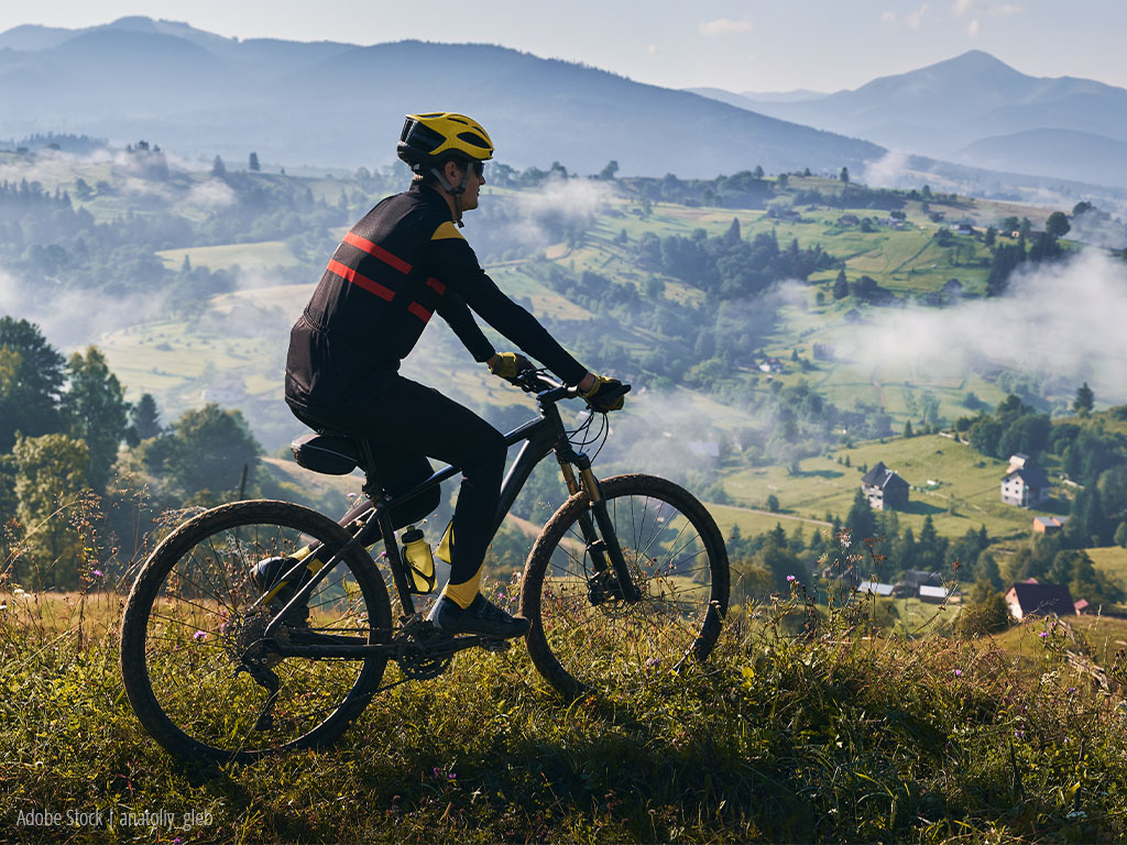 a man rides his bike across a meadow, mountains can be seen in the background