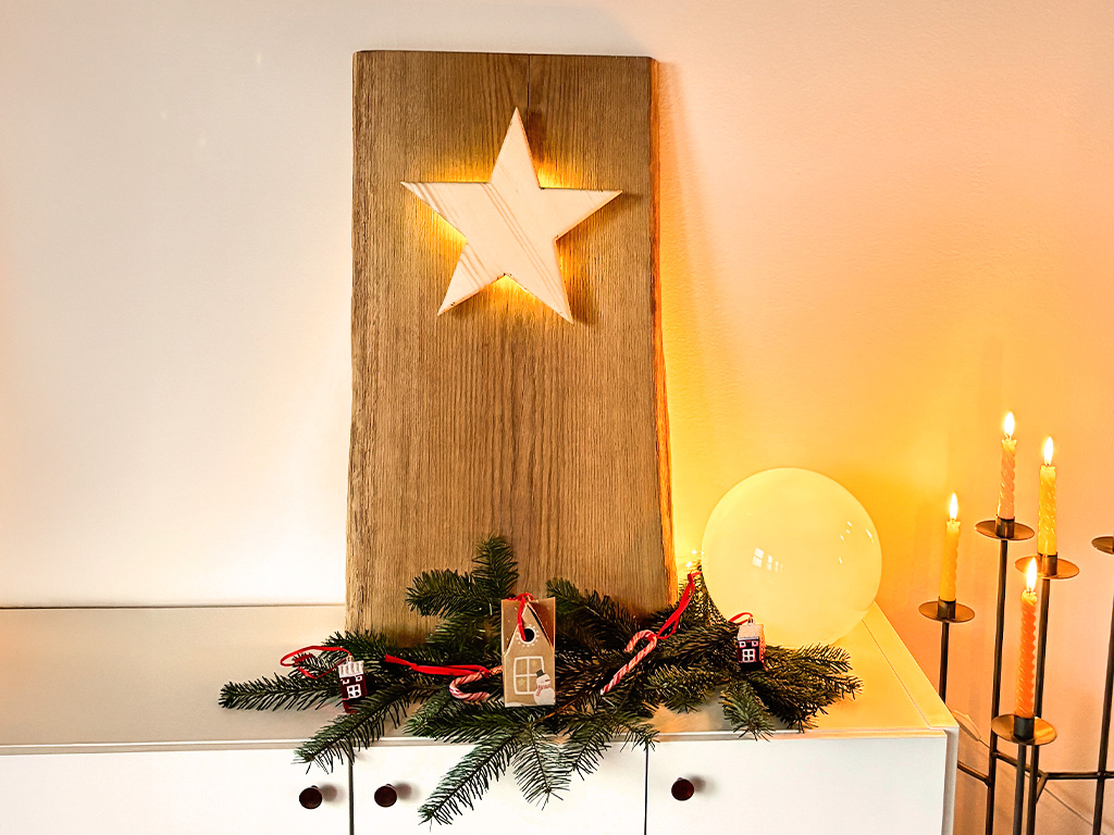 Ein beleuchteter Holzstern ist in eine große Holzplatte eingelassen, dekoriert mit Tannenzweigen und Kerzen.