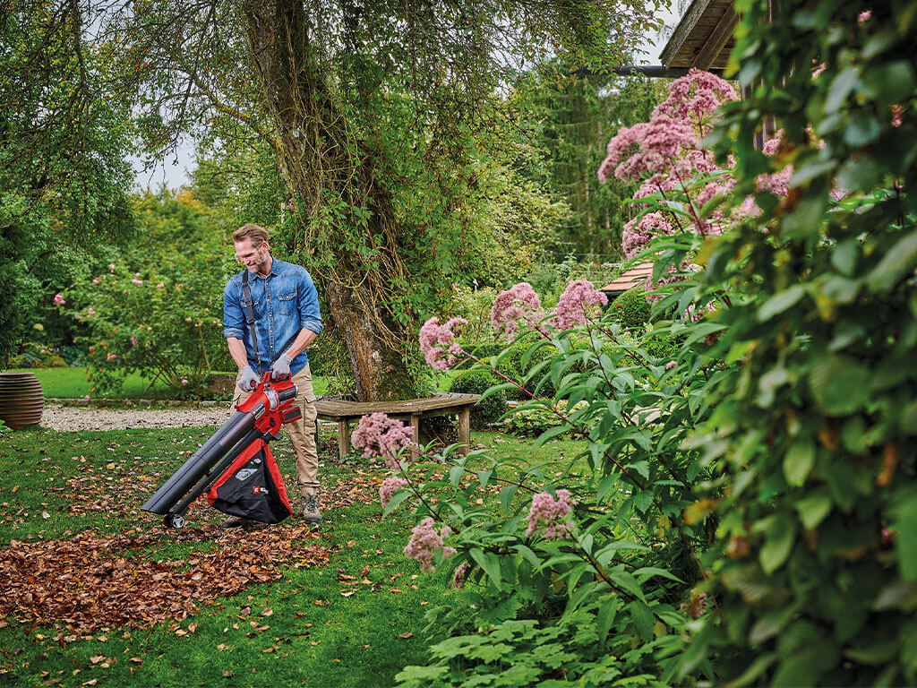 Ein Mann befreit mit Hilfe eines Einhell Laubsaugers seinen Garten von Herbstlaub.