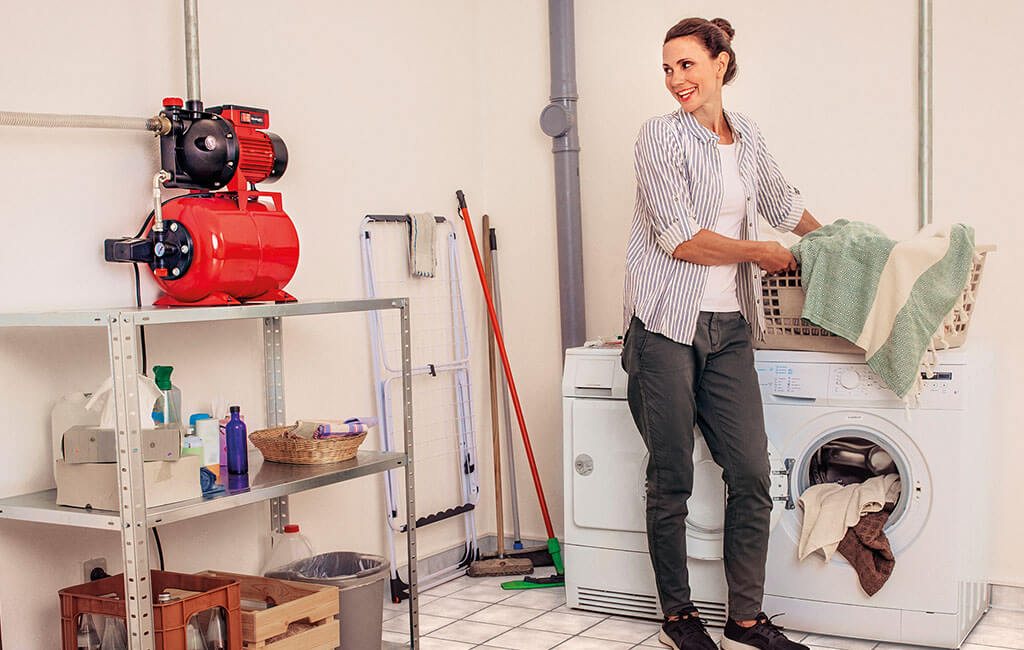 A woman emptying a washing machine which is connected to a water works.