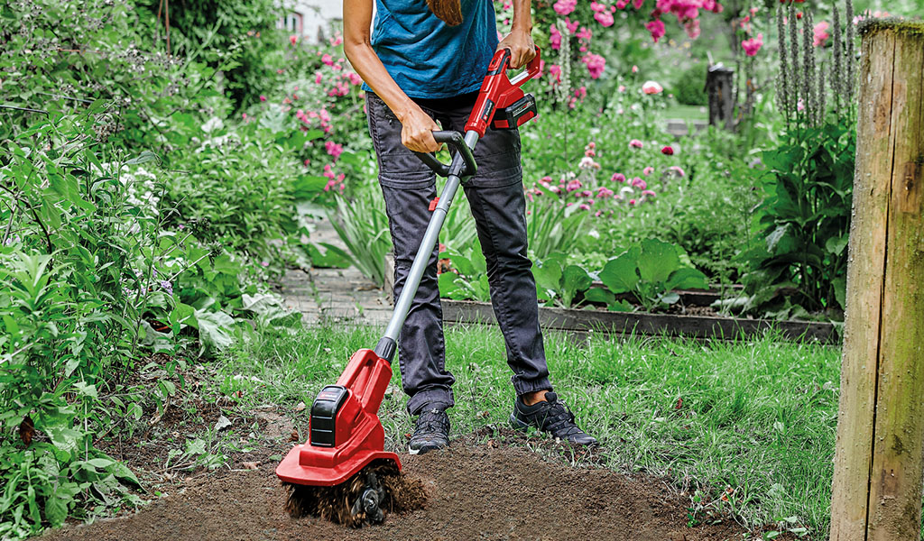 A woman uses a cordless tiller from Einhell in the garden