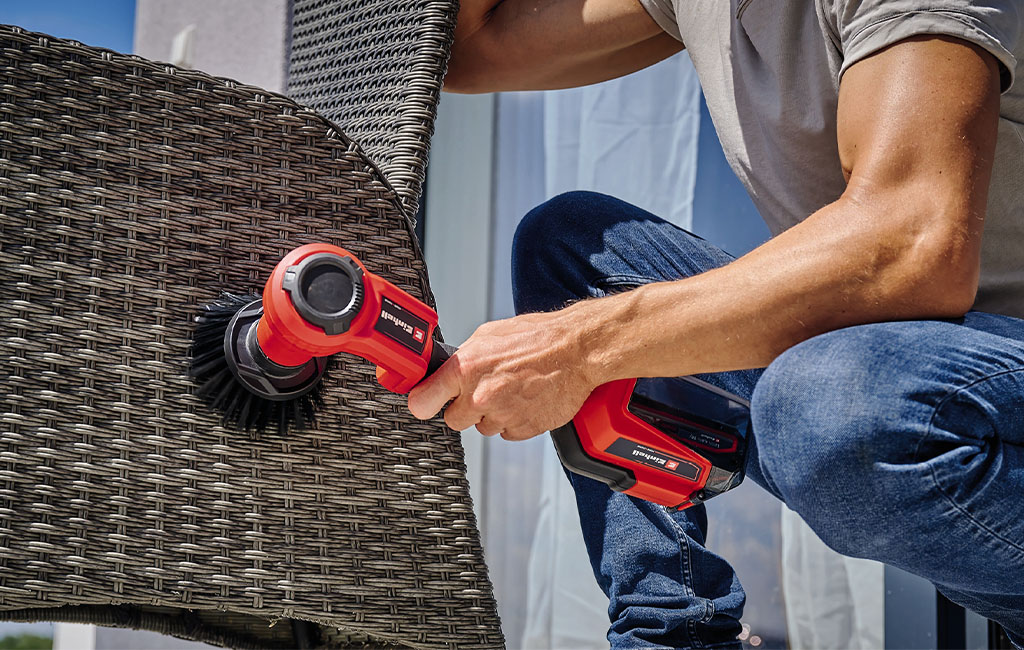 Man cleaning rattan garden chair with a cordless surface brush with a soft, rotating brush