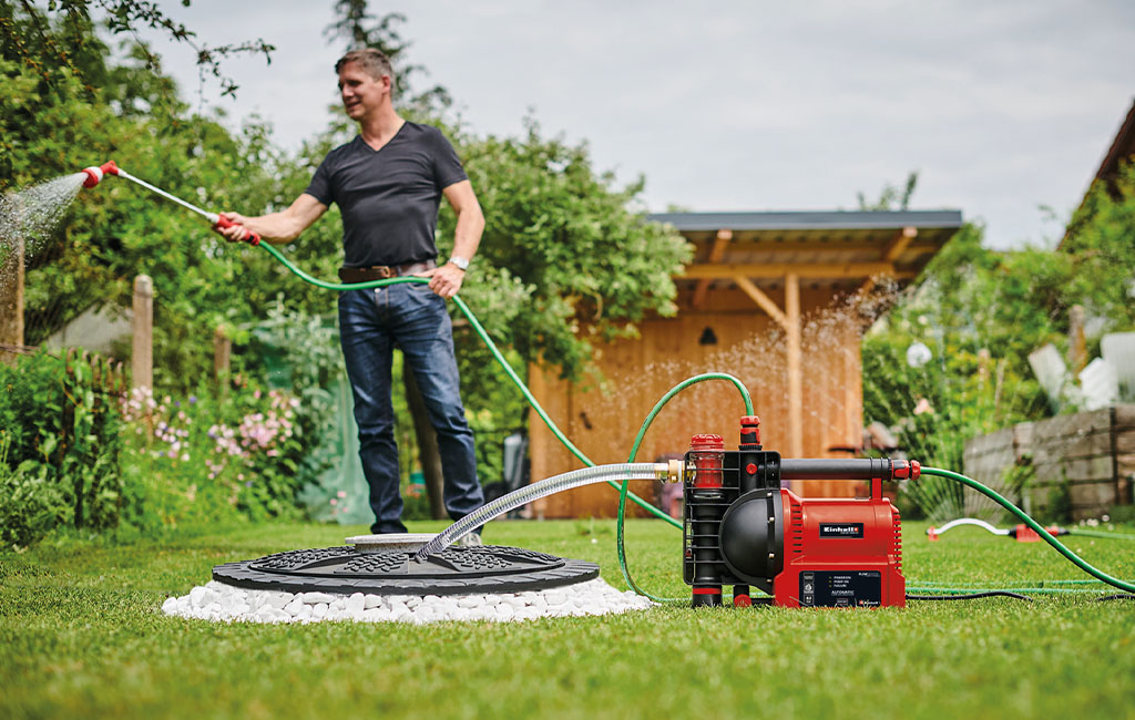 Ein Mann spritzt Wasser in einem Garten mit einer automatischen Gartenpumpe im Vordergrund.