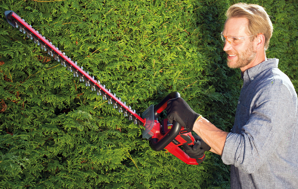 ein Mann schneidet mit einer Einhell Akku-Heckenschere eine Hecke