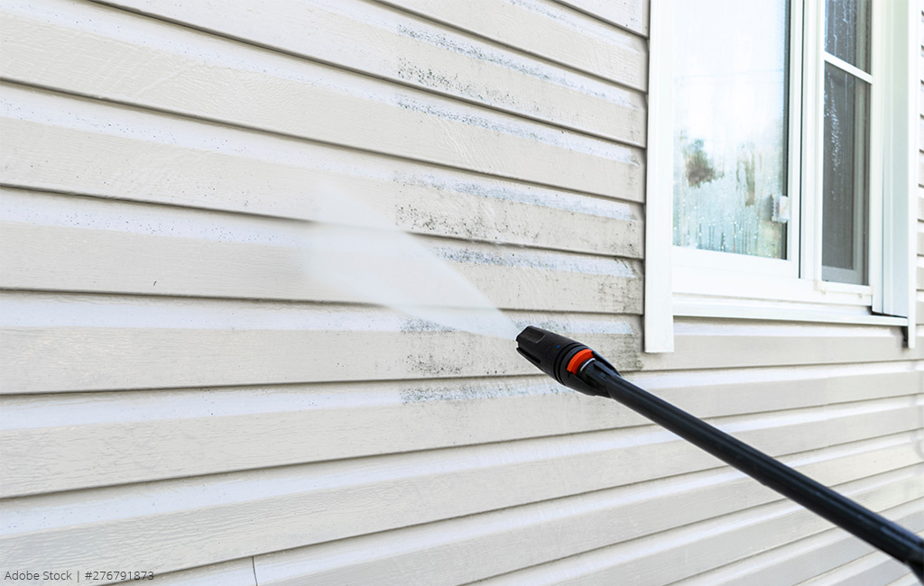 A close-up of a pressure washer removing dirt from the exterior wall of a house.