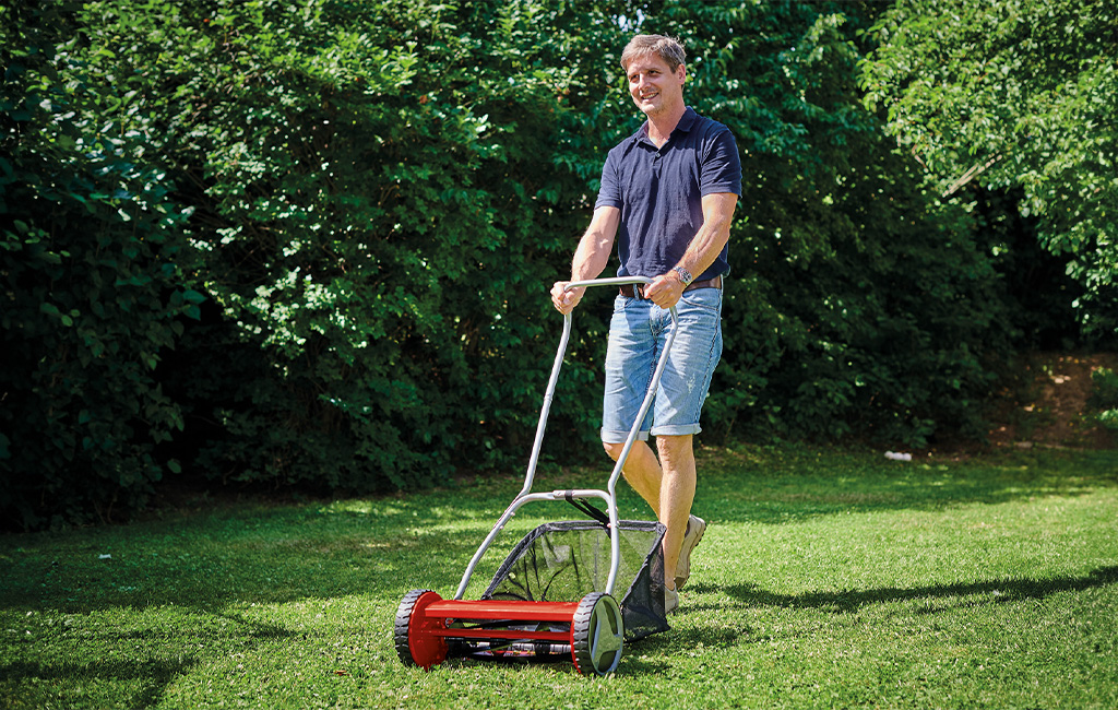 A man mowing the lawn with a hand mower. 