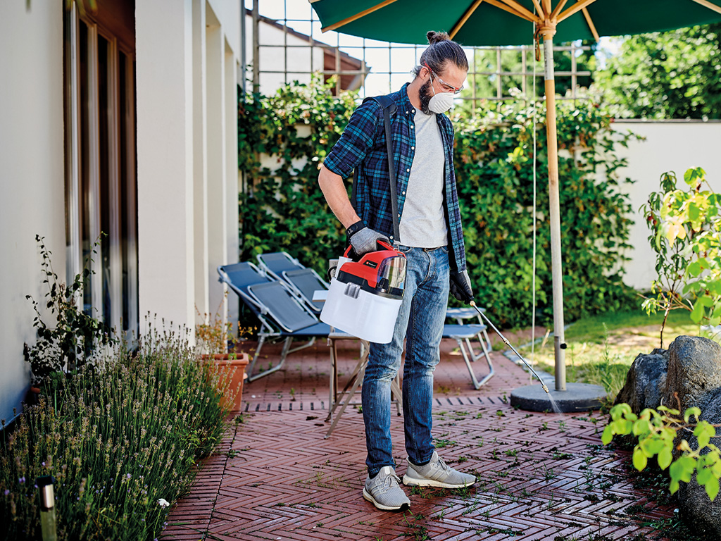 a man is removing weeds using an Einhell cordless pressure sprayer