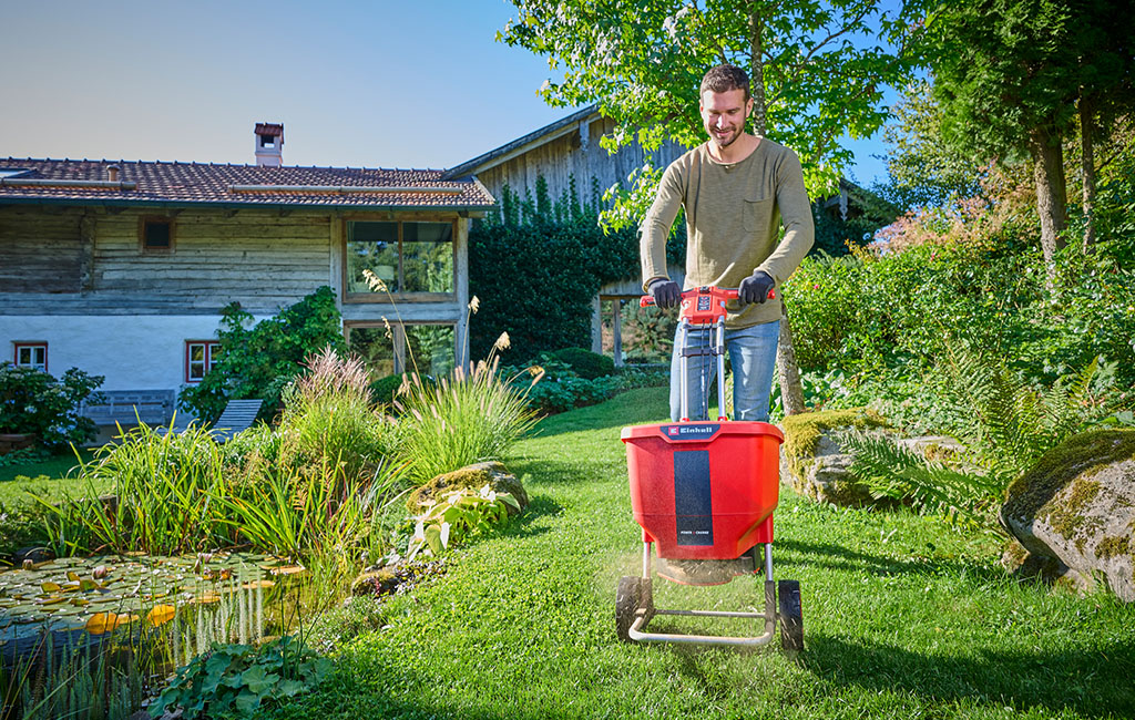 A man with an Einhell cordless spreader distributing fertiliser in the garden