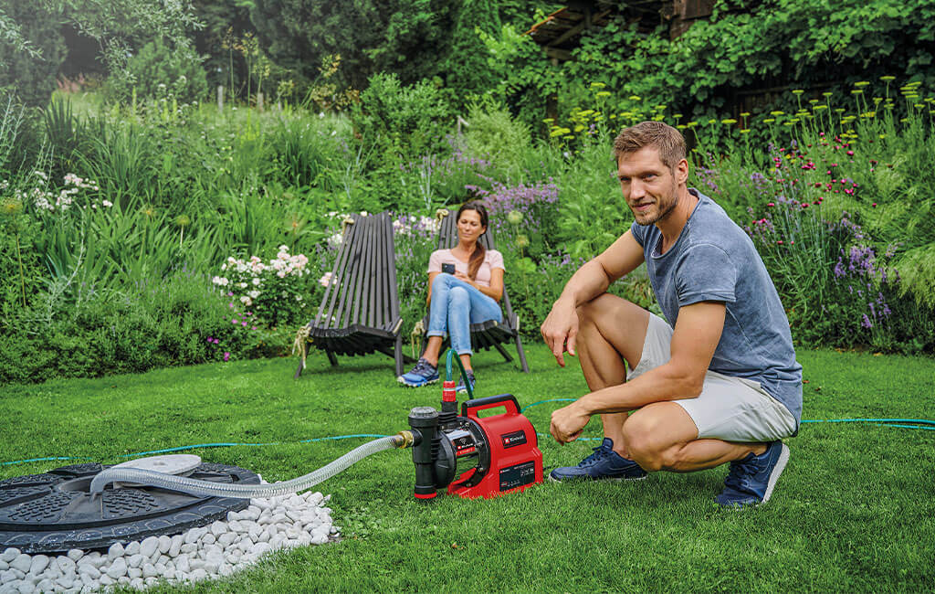 A man kneeling and a woman sitting next to a garden pump in their garden.