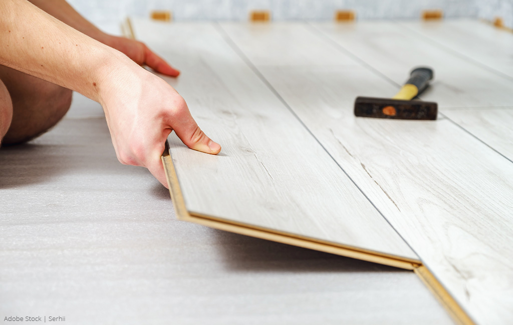 Two hands clicking laminate planks together, assisted by a hammer.