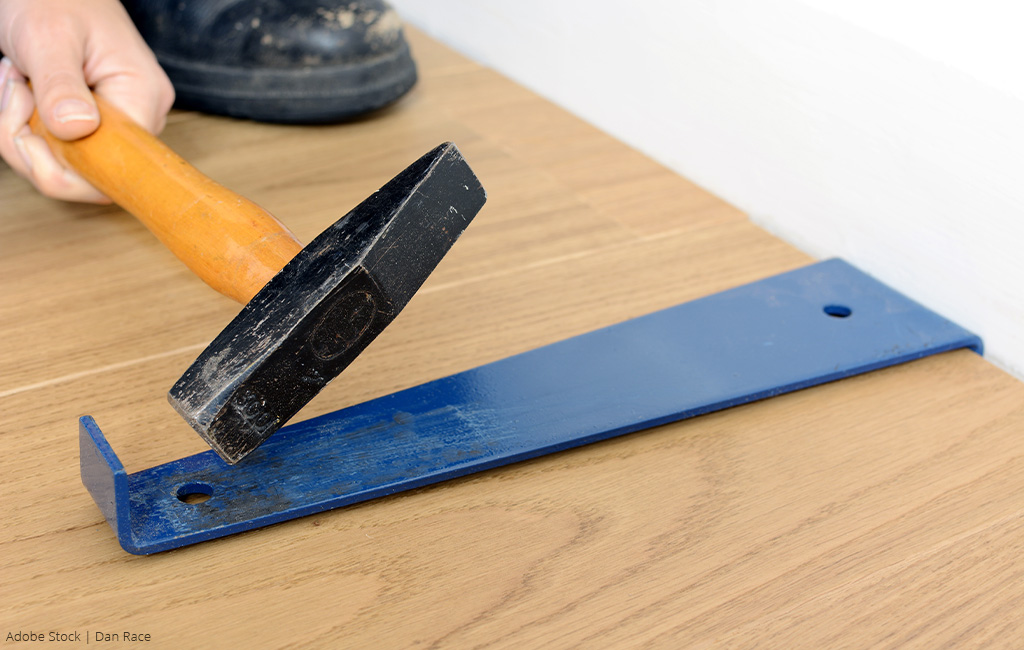 A hammer and a pull bar are used to install laminate flooring.