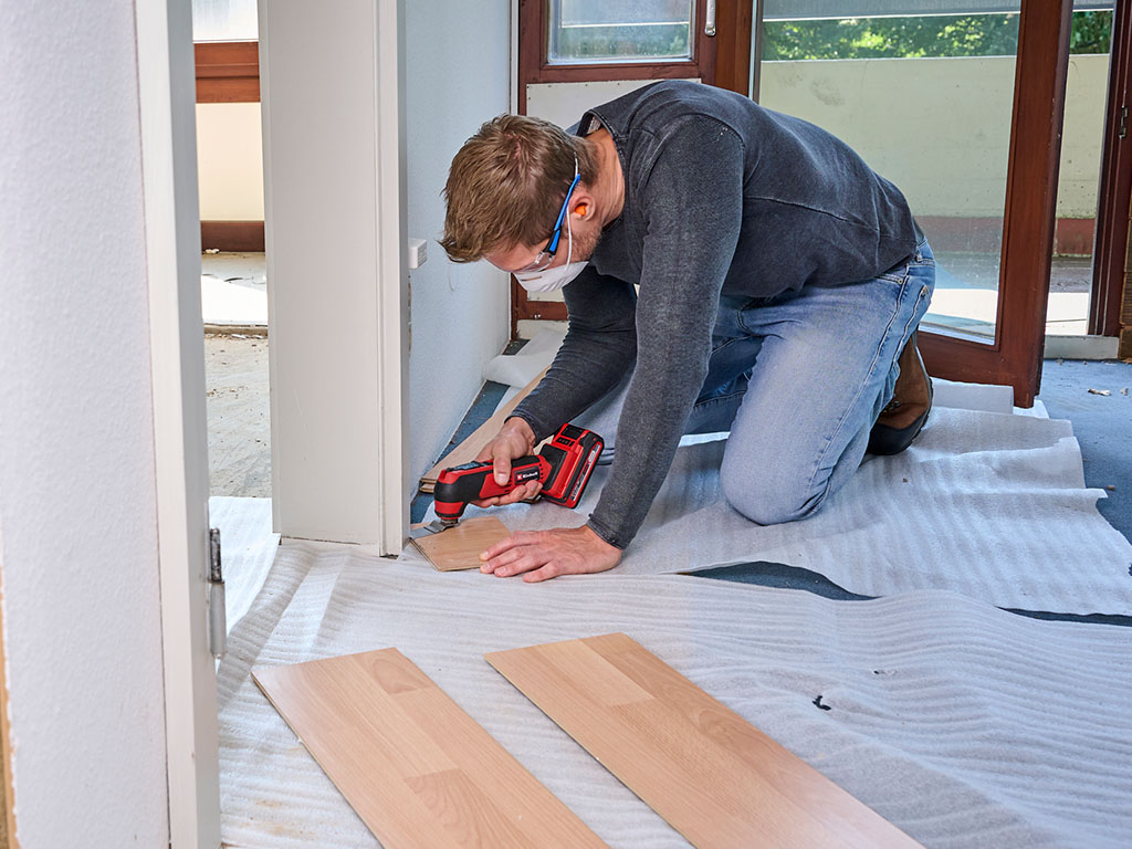 A man using an Einhell cordless multitool to cut laminate planks in a room during renovation.