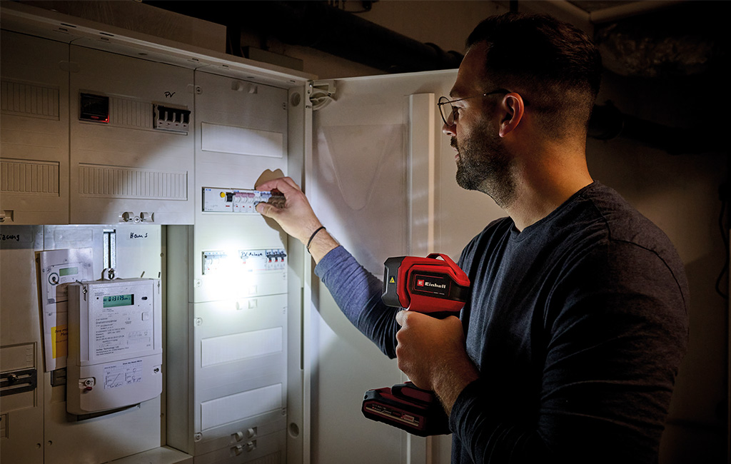 A man lights up an electrical panel with an Einhell cordless work light while checking a fuse.