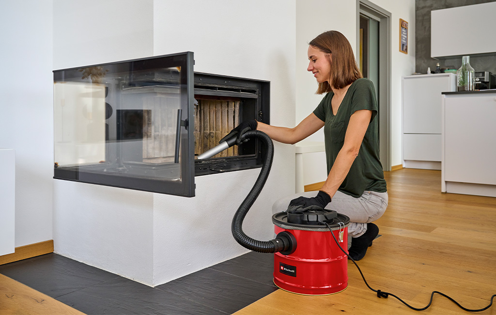 A woman using an Einhell ash vacuum to clean the firebox of a fireplace.