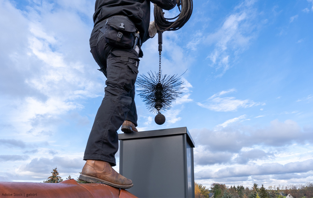 A chimney sweep cleaning a chimney with a brush on a rooftop.