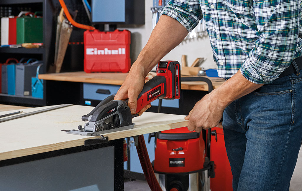 Ein Mann schneidet Holz mit einer Einhell Handkreissäge auf einer Werkbank.