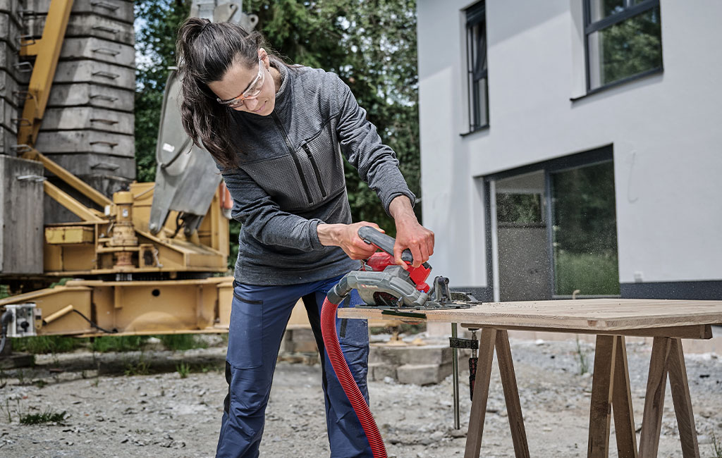 Eine Frau mit Schutzbrille benutzt eine Handkreissäge, um Holz auf einer Baustelle zu schneiden.