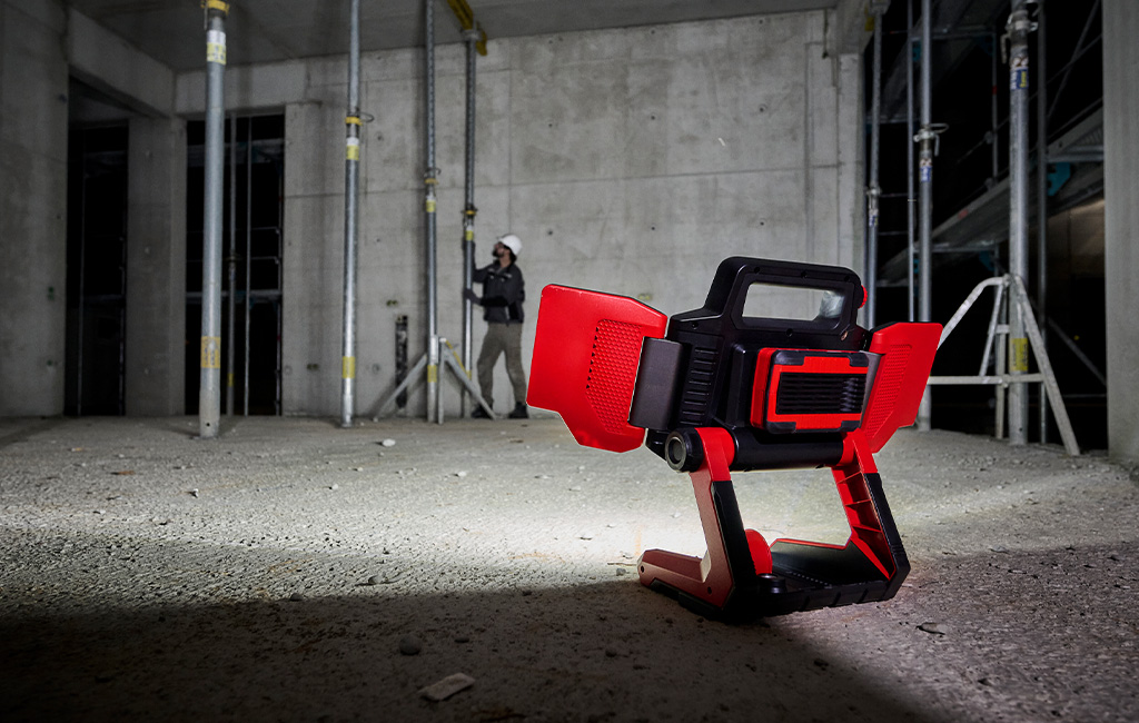 A Einhell portable LED work light illuminates a construction site as a person works on a support in the background.