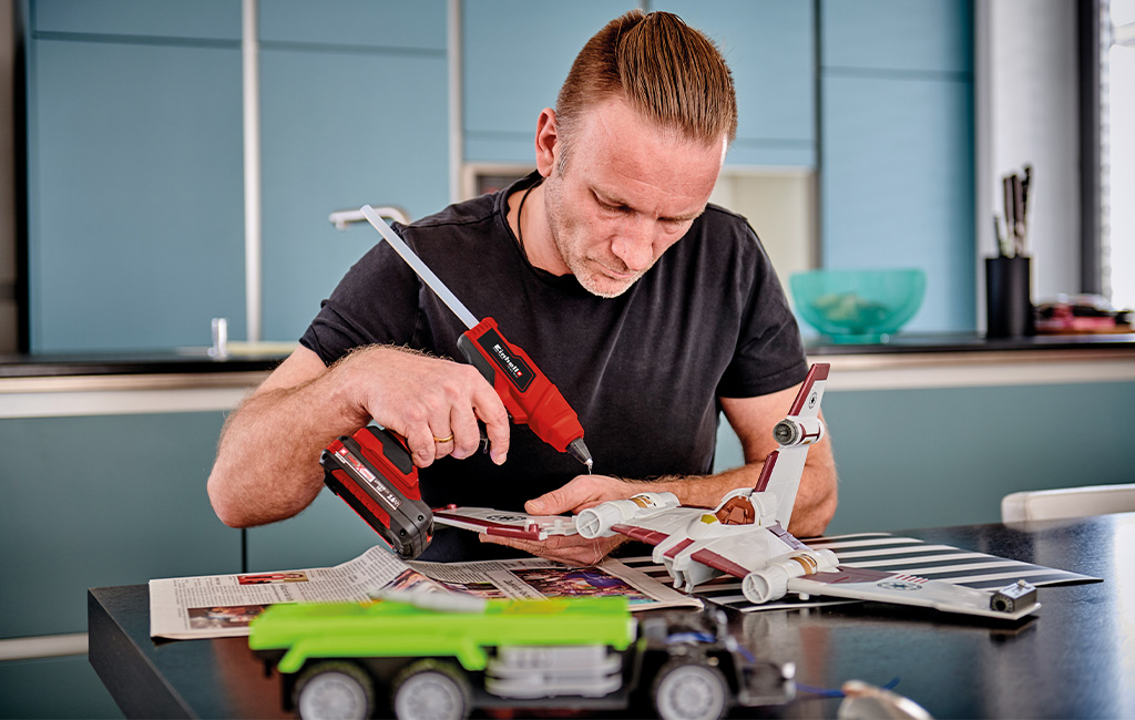 A man uses a cordless hot glue gun to build a model spaceship.