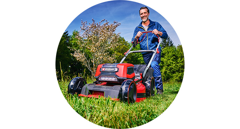 A man mows a lawn with a cordless Einhell lawn mower on a sunny day.