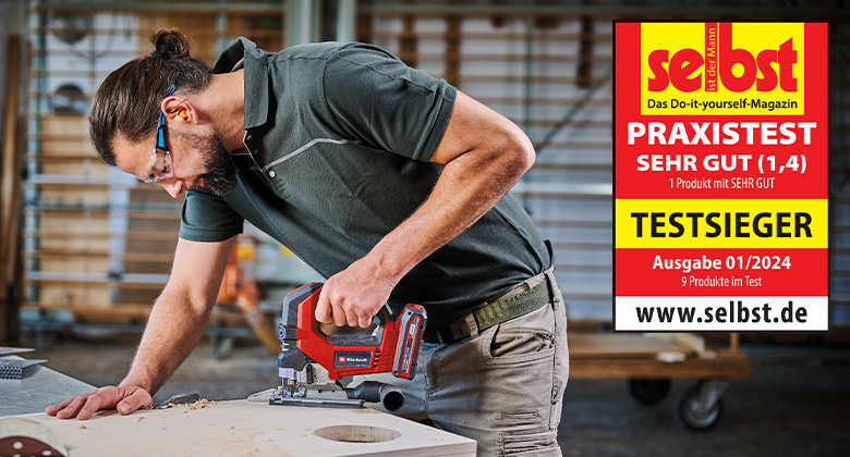 A man uses an Einhell cordless jigsaw in a workshop, rated "Very Good" (1.4) and awarded as the test winner in the practical test by "selbst ist der Mann" in issue 01/2024.