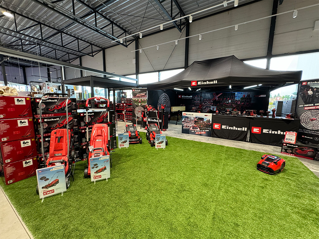 Einhell indoor setup with lawn care equipment displayed on artificial grass and promotional materials.