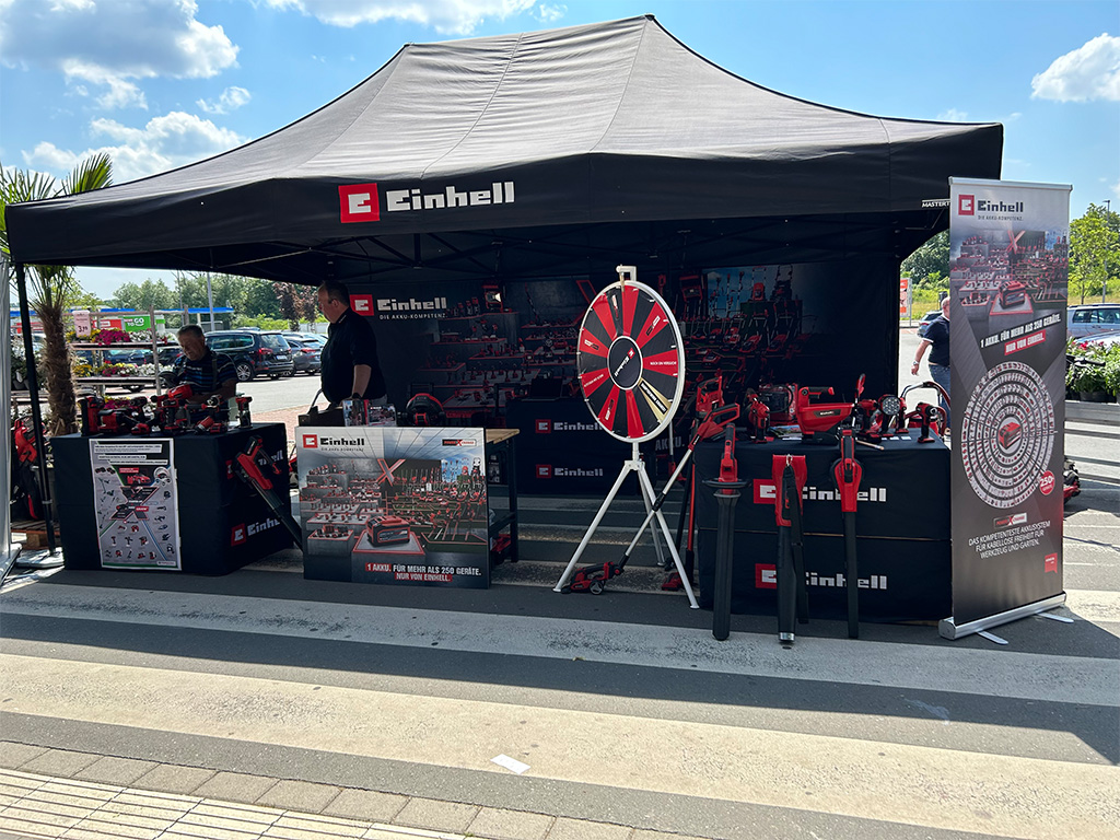 Outdoor Einhell promotional tent with a spinning wheel and product displays, set in a parking lot.