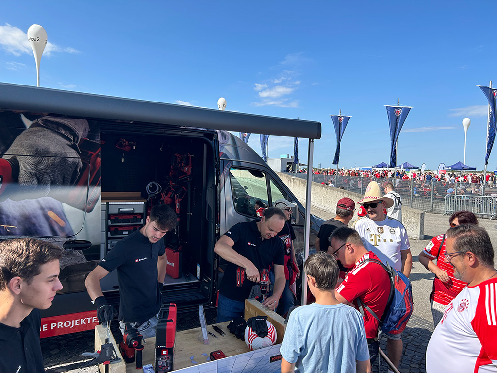 Einhell van with team members demonstrating tools to visitors outdoors under a sunny sky.