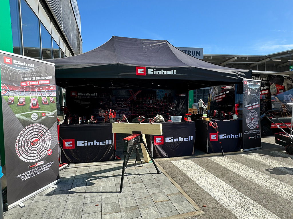 Einhell outdoor tent set up in front of a hardware store, featuring tools, banners, and demonstration setups.