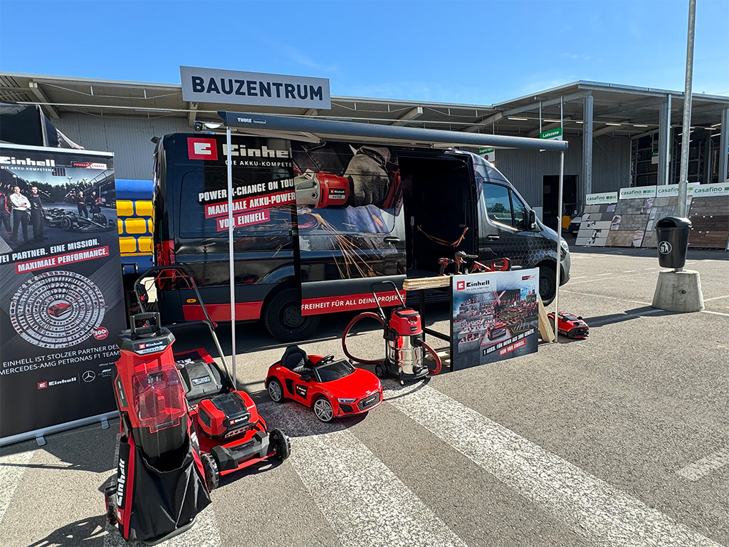 Einhell outdoor promotional setup with displayed lawn equipment, banners, and tools near a hardware store.