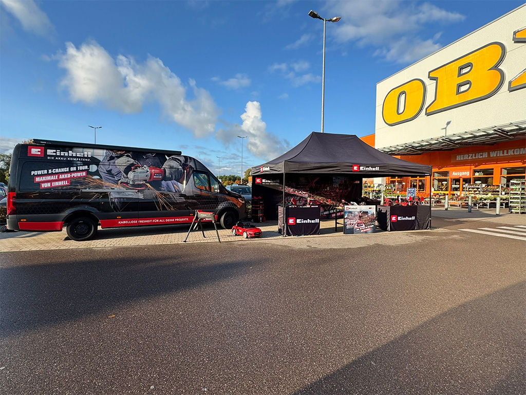 Einhell outdoor booth in front of an OBI hardware store, featuring tools, banners, and a promotional van.